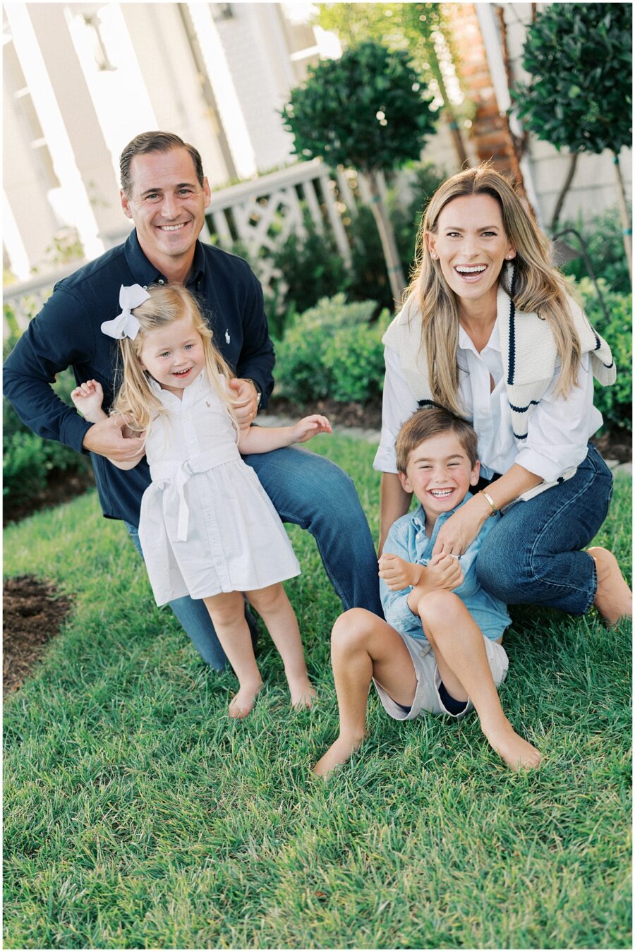 Family with a 2 year old girl and 4 year old boy laughing in the grass at their home.