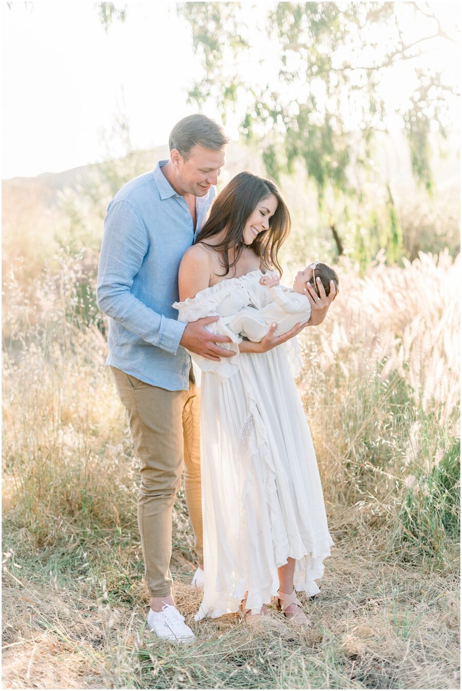 New parents holding newborn baby girl in grassy field smiling at her in Irvine
