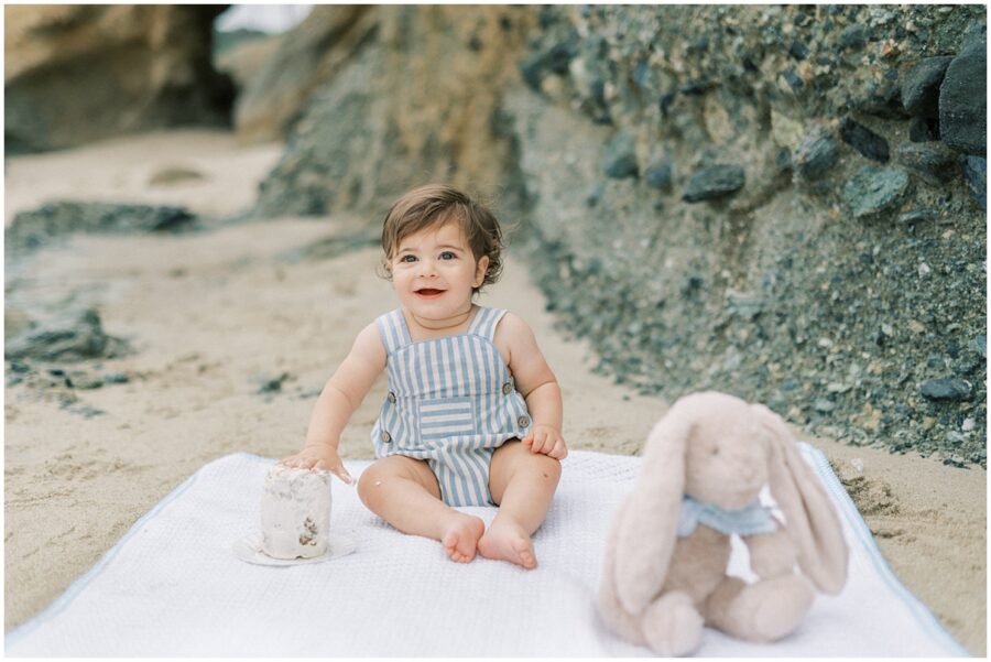 baby sitting on the beach with hand in cake in Laguna Beach for 1st birthday