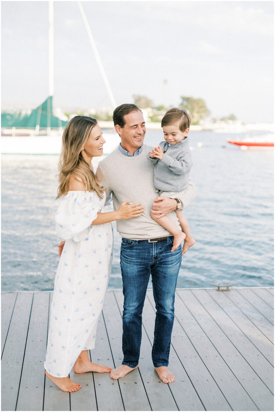 mom and dad holding little boy on a dock in Balboa Beach by sailboats
