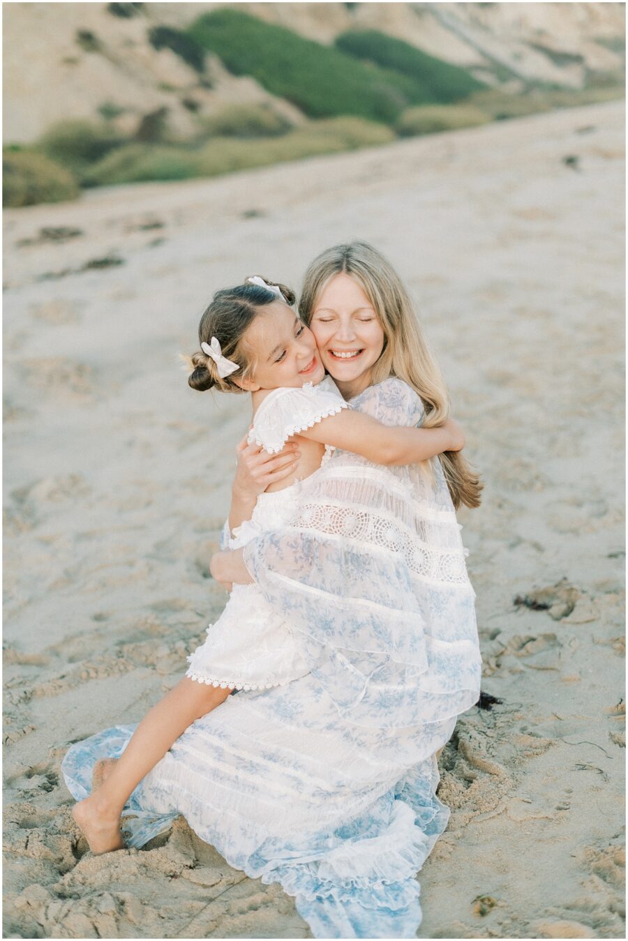 mom hugging 4 year old daughter on beach smiling