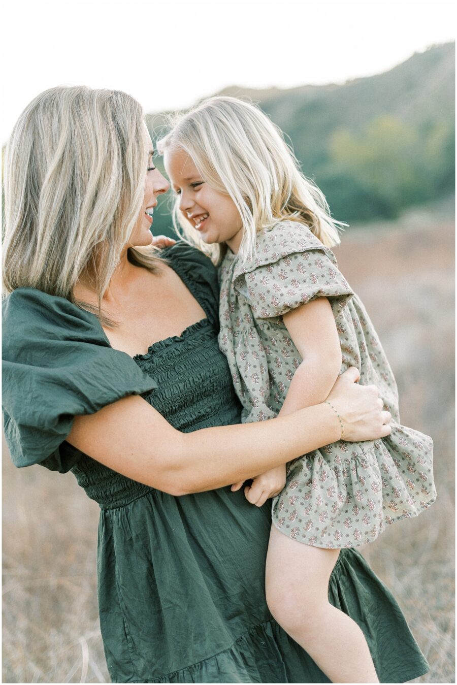 mom holding daughter laughing in green dress in fall in orange county ca.