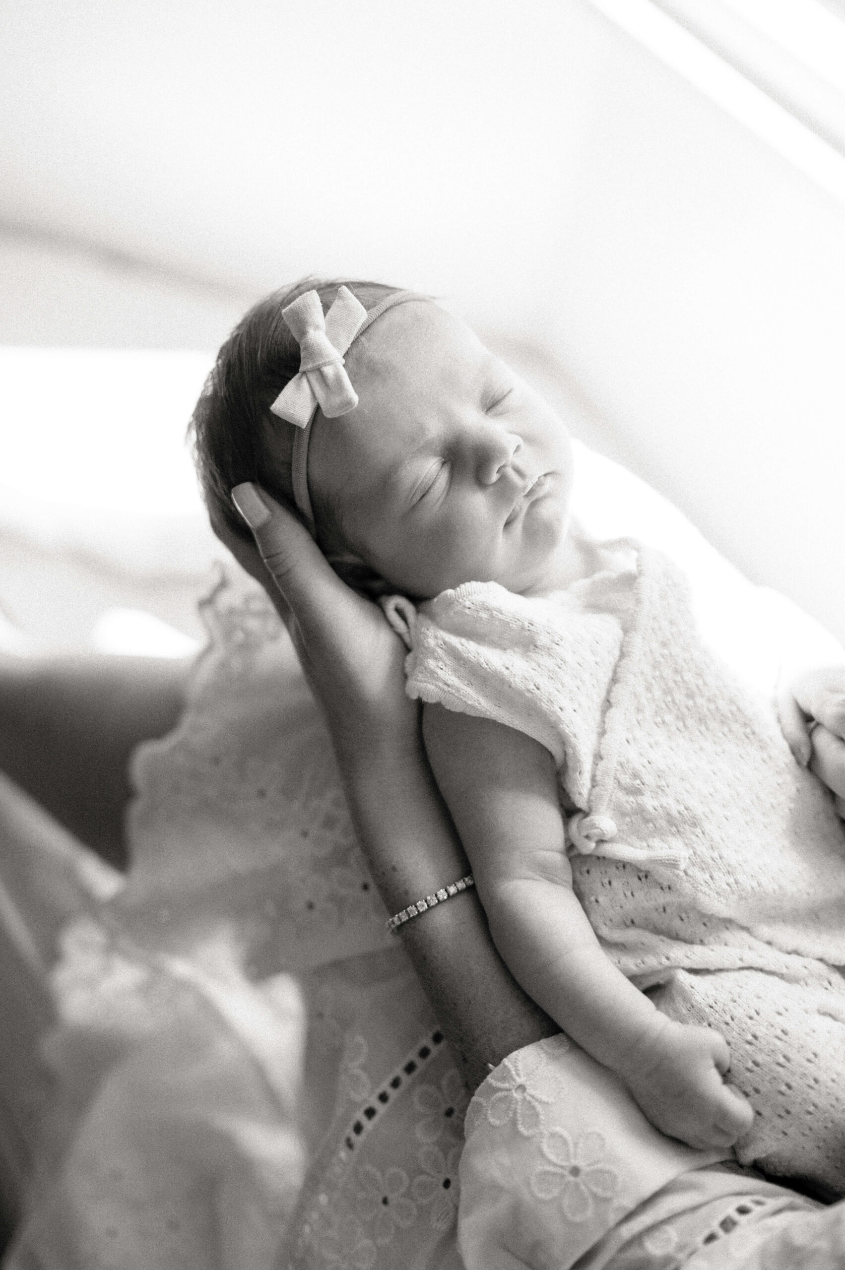 A newborn baby sleeps in a dress in black and white in mom's hands